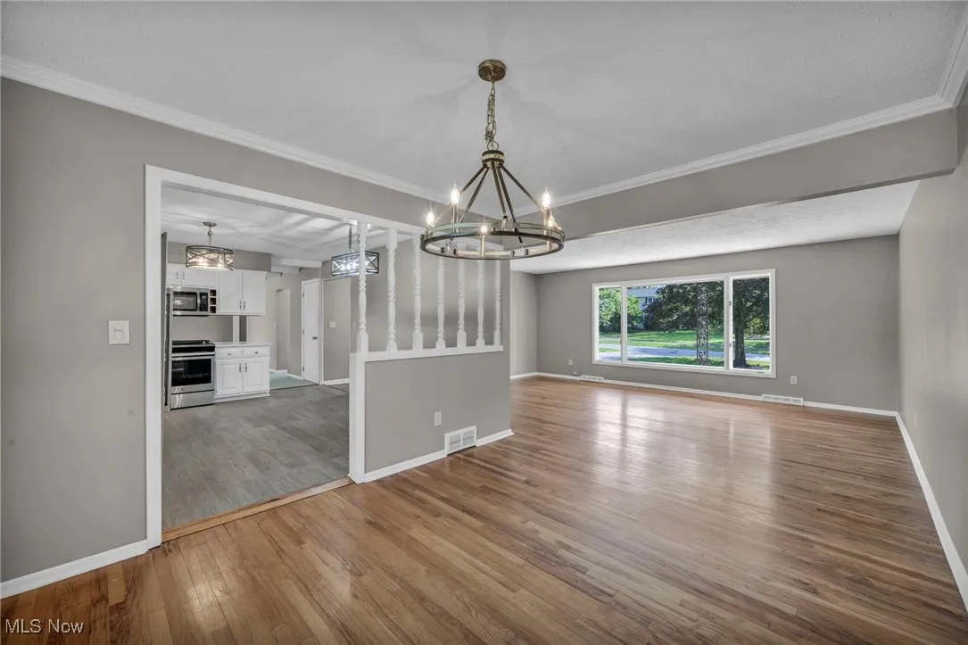 Unfurnished dining area featuring dark wood-style flooring, ornamental molding, and a chandelier