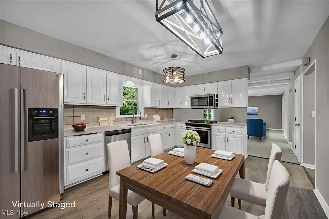 Kitchen with appliances with stainless steel finishes, white cabinets, backsplash, and hanging light fixtures