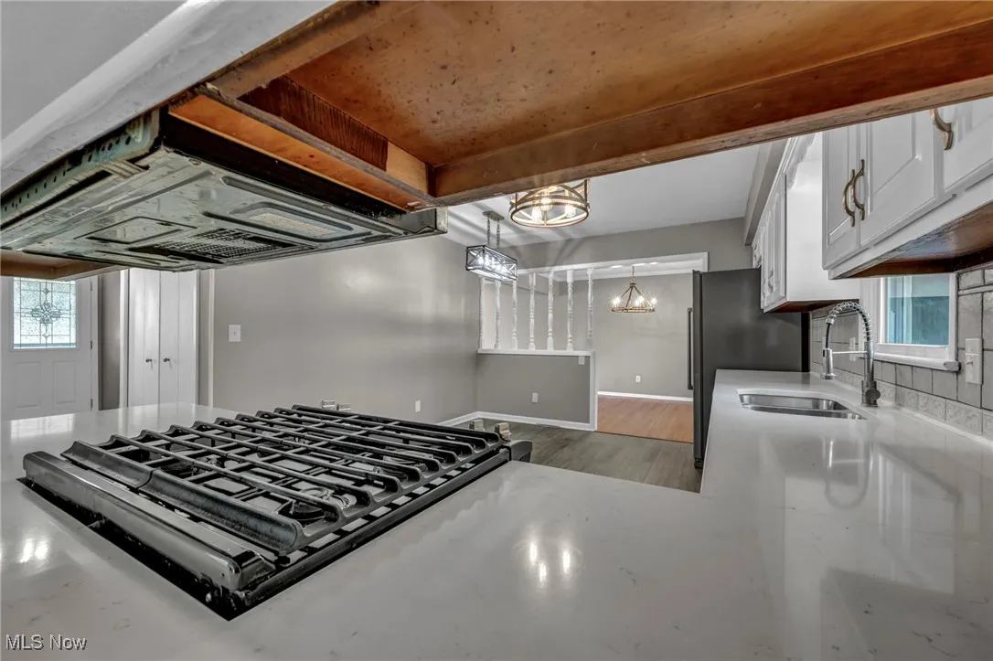 Kitchen with range hood, black gas cooktop, white cabinets, light stone counters, and wood finished floors