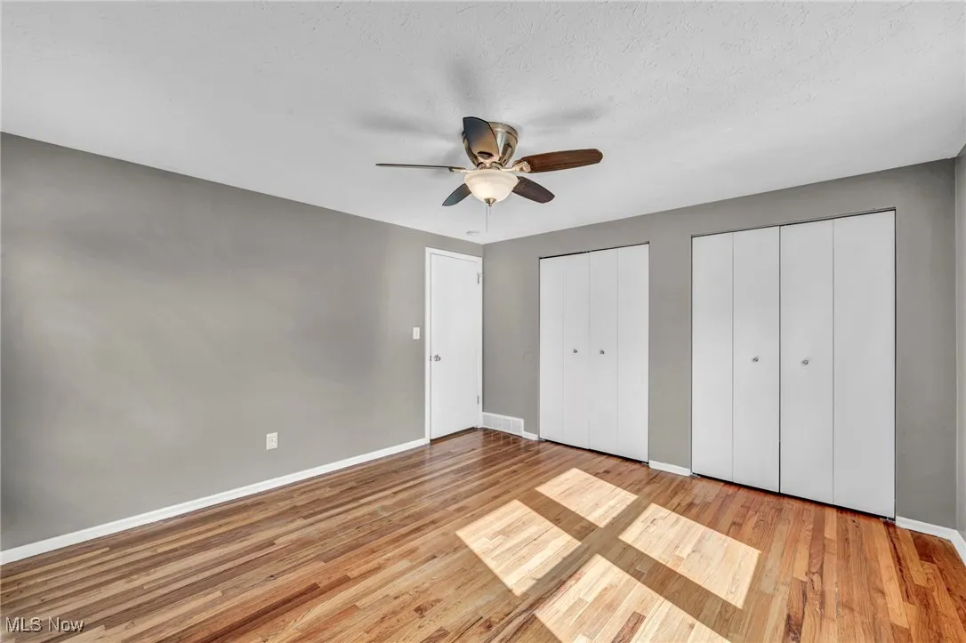 Unfurnished bedroom featuring two closets, light wood-type flooring, a ceiling fan, and a textured ceiling