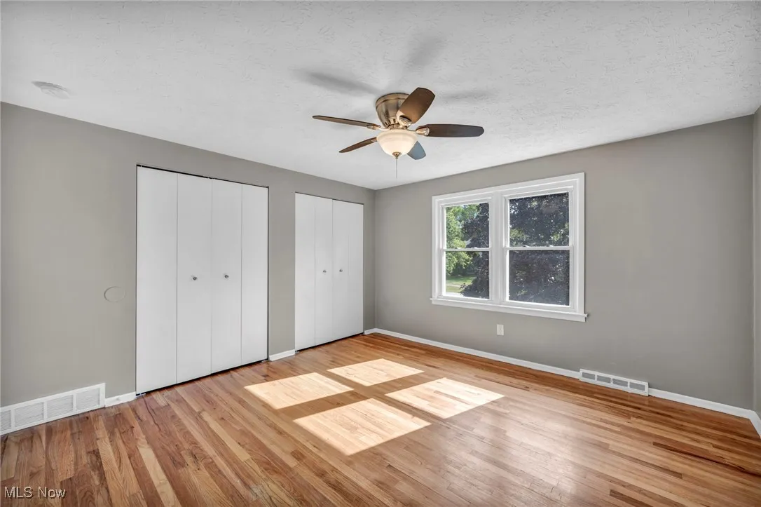 Unfurnished bedroom with multiple closets, light wood-style flooring, a ceiling fan, and a textured ceiling