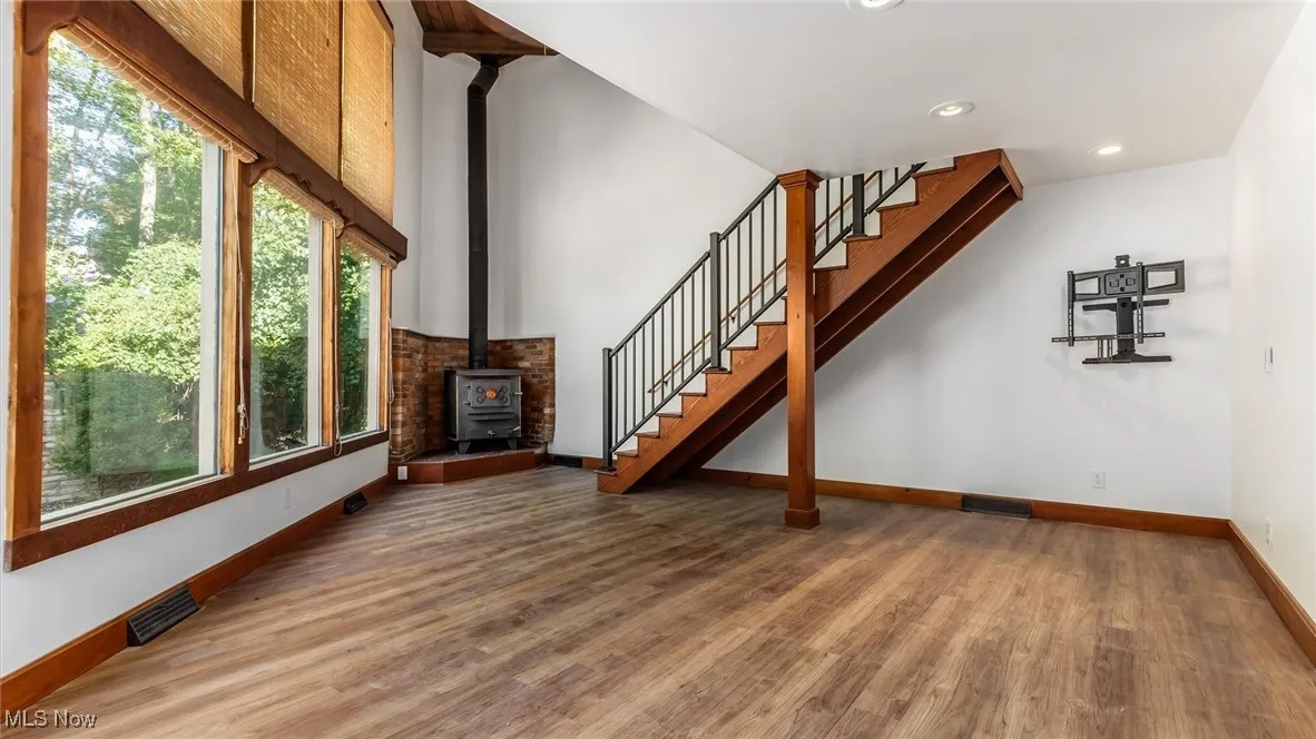 Unfurnished living room with a wood stove, wood finished floors, stairway, and recessed lighting