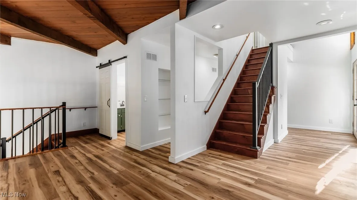 Stairway featuring a barn door, wood finished floors, a wooden ceiling with exposed beams, and recessed lighting