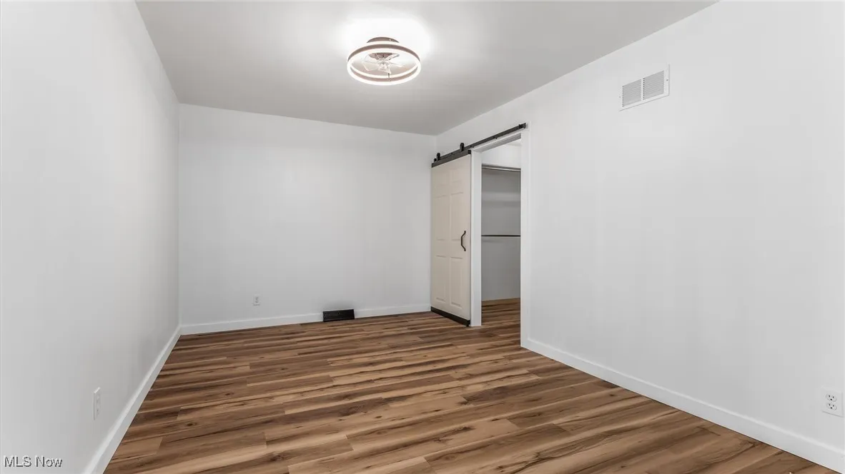 Unfurnished bedroom featuring a spacious closet, wood finished floors, and a barn door