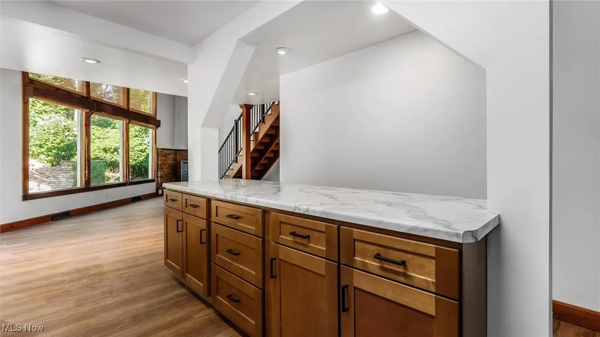 Bar featuring brown cabinetry, light wood-style flooring, recessed lighting, and stairs