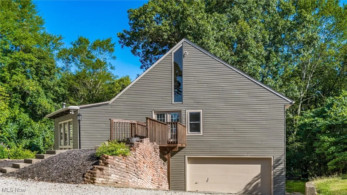 View of side of home featuring an attached garage, driveway, and a deck