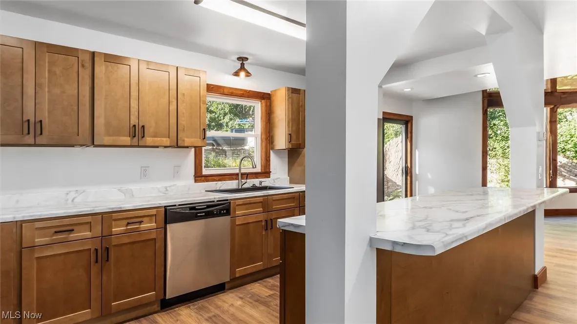Kitchen featuring brown cabinetry, light wood-style flooring, stainless steel dishwasher, and light stone counters
