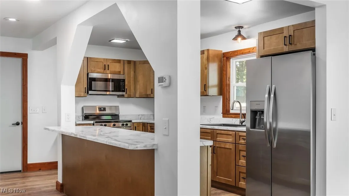 Kitchen with brown cabinets, stainless steel appliances, light wood finished floors, and light stone counters