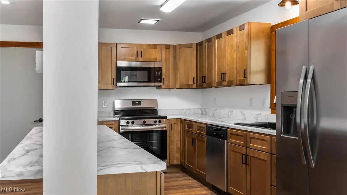 Kitchen with appliances with stainless steel finishes, dark wood-style flooring, and brown cabinets