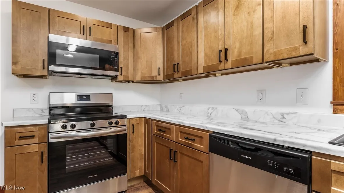 Kitchen with stainless steel appliances, brown cabinetry, light countertops, and dark wood-style floors