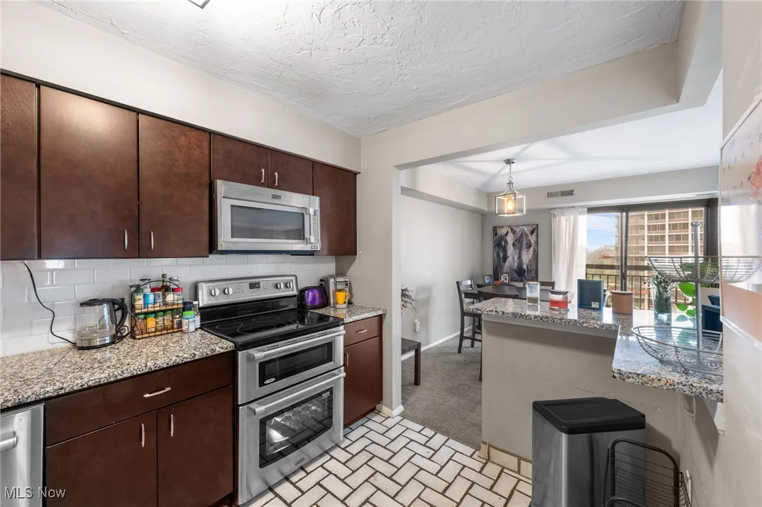 Kitchen featuring dark brown cabinets, appliances with stainless steel finishes, decorative backsplash, and stone countertops