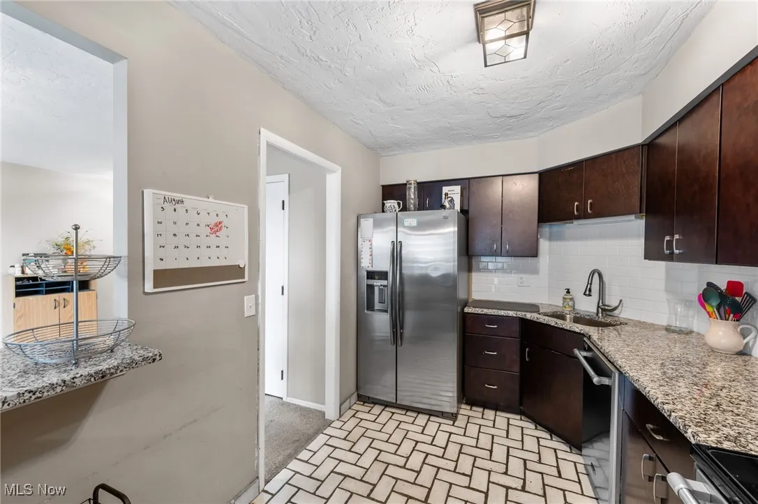 Kitchen with dark brown cabinetry, stainless steel appliances, decorative backsplash, a textured ceiling, and light stone counters