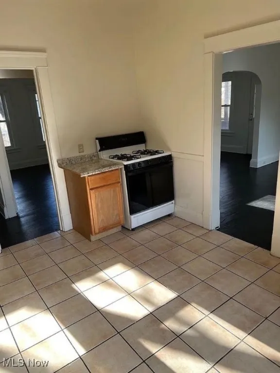 Kitchen with arched walkways, white range with gas cooktop, light tile patterned flooring, and brown cabinetry