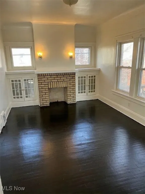 Unfurnished living room with dark wood-style flooring and a brick fireplace