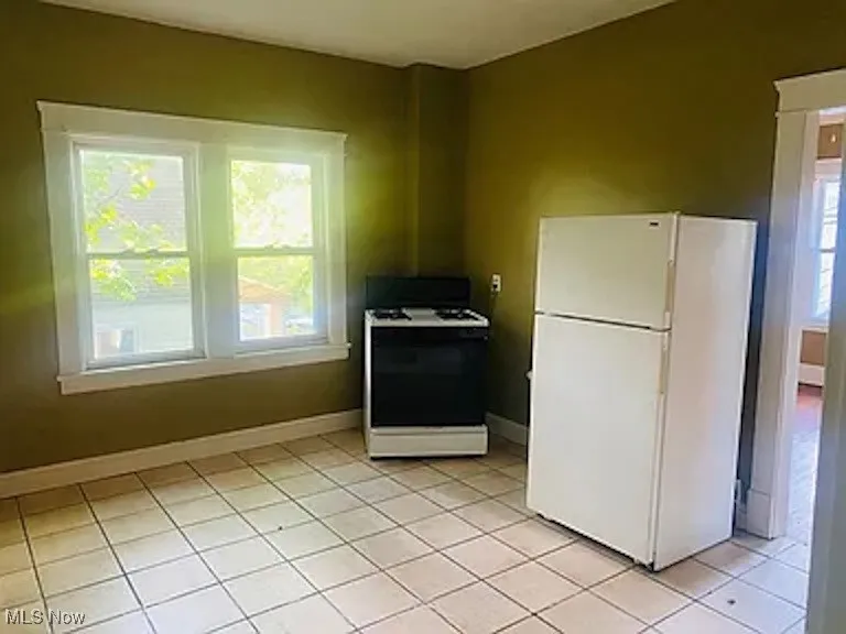 Kitchen with freestanding refrigerator, range with gas stovetop, and light tile patterned flooring