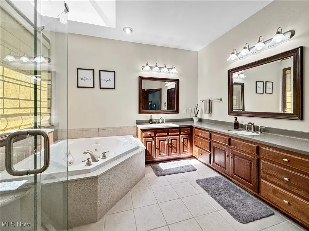 Full bathroom featuring double vanity, a whirlpool tub, light tile patterned floors, a shower stall, and a skylight