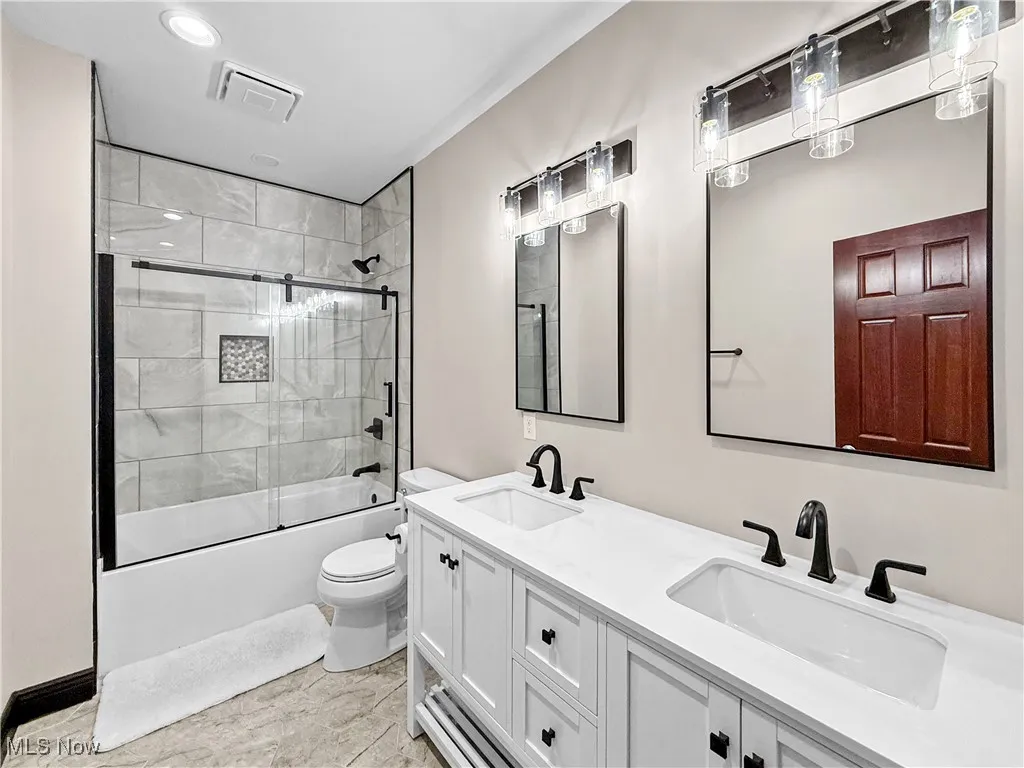 Full bath with enclosed tub / shower combo, double vanity, and recessed lighting