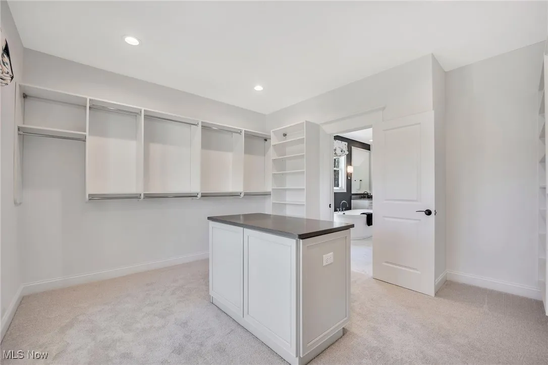 Primary Walk in closet with custom shelving, island and light carpet