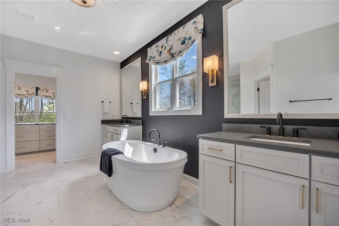 Primary bathroom with separate vanities, a freestanding bath, light marble finish floors, quartz countertops and recessed lighting