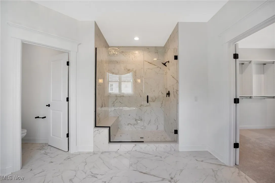 Bathroom featuring a marble tile shower, light marble finish flooring, recessed lighting, and a spacious closet