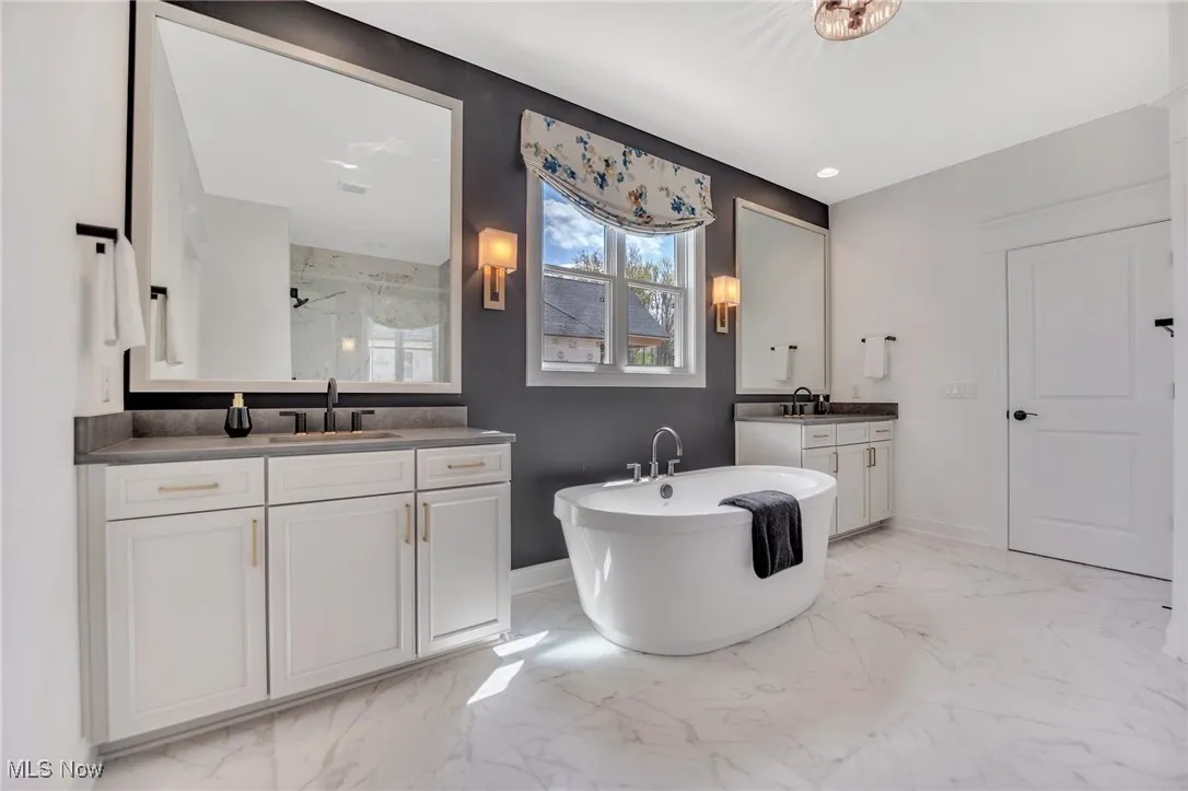 Primary bathroom with separate vanities, a freestanding bath, light marble finish floors, quartz countertops and recessed lighting