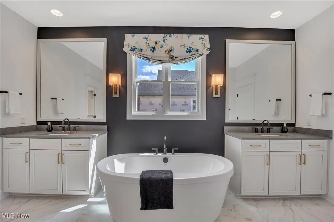 Primary bathroom with separate vanities, a freestanding bath, light marble finish floors, quartz countertops and recessed lighting