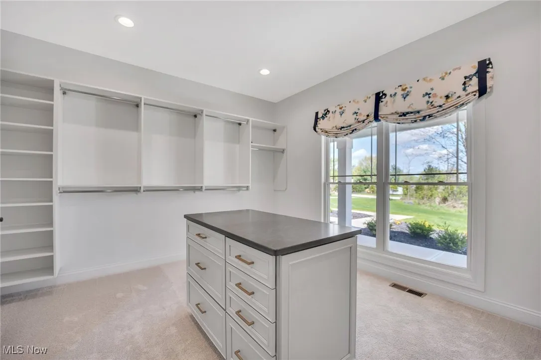 Primary Walk in closet with custom shelving, island and light carpet