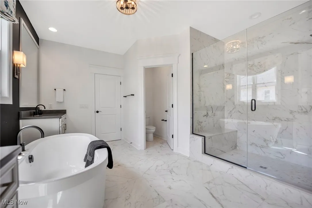 Bathroom with light marble finish flooring, vanity, a freestanding bath, a marble finish shower, and recessed lighting