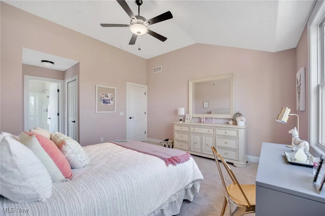 Bedroom featuring ensuite bath, vaulted ceiling, light carpet, ceiling fan and a private bath
