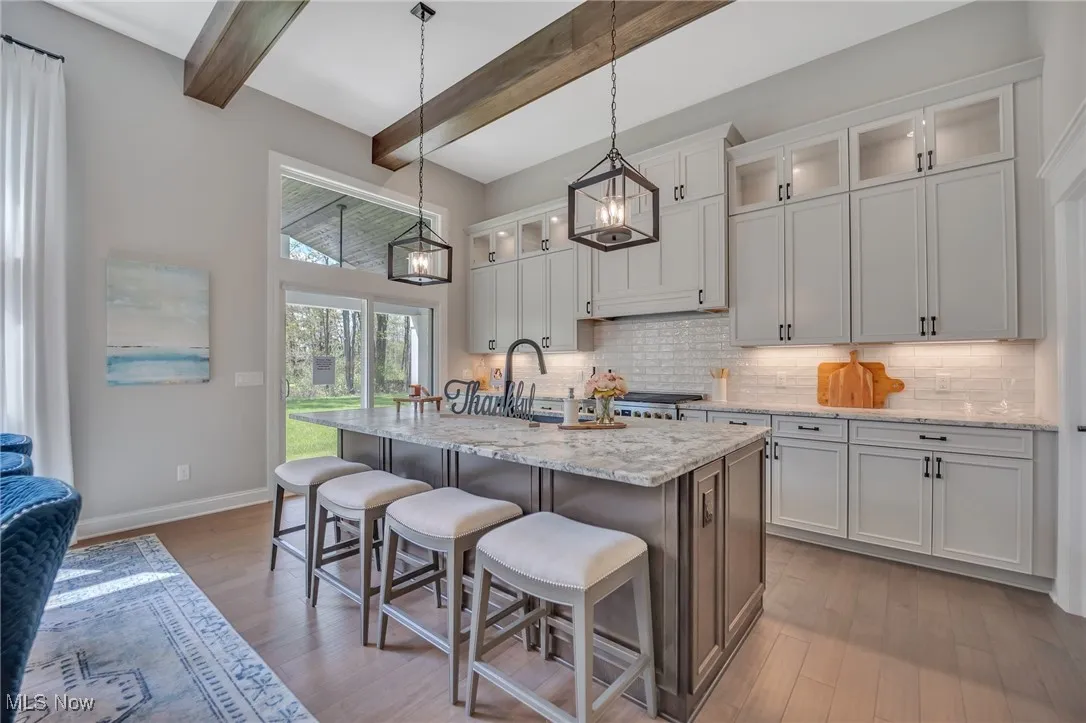 Kitchen featuring glass insert cabinets, a breakfast bar, tile backsplash, hardwood flooring, and leather finished granite counters