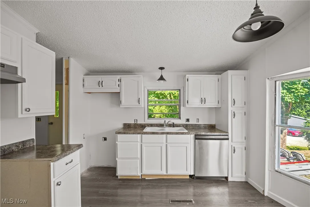 Kitchen with dark wood-type flooring, dishwasher, a textured ceiling, dark countertops, and white cabinets