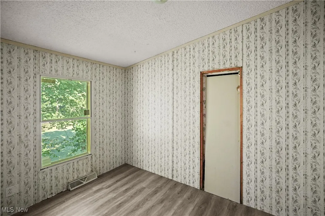 Unfurnished room with wood finished floors, a textured ceiling, and crown molding