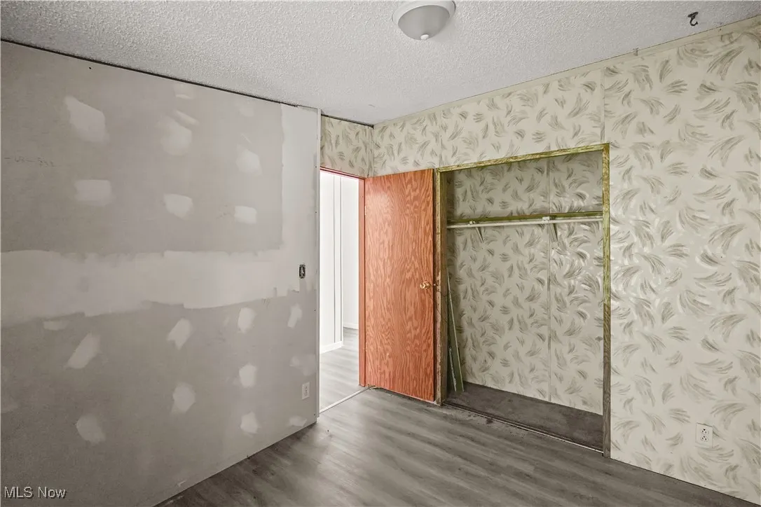 Unfurnished bedroom featuring dark wood-type flooring, a textured ceiling, and wallpapered walls