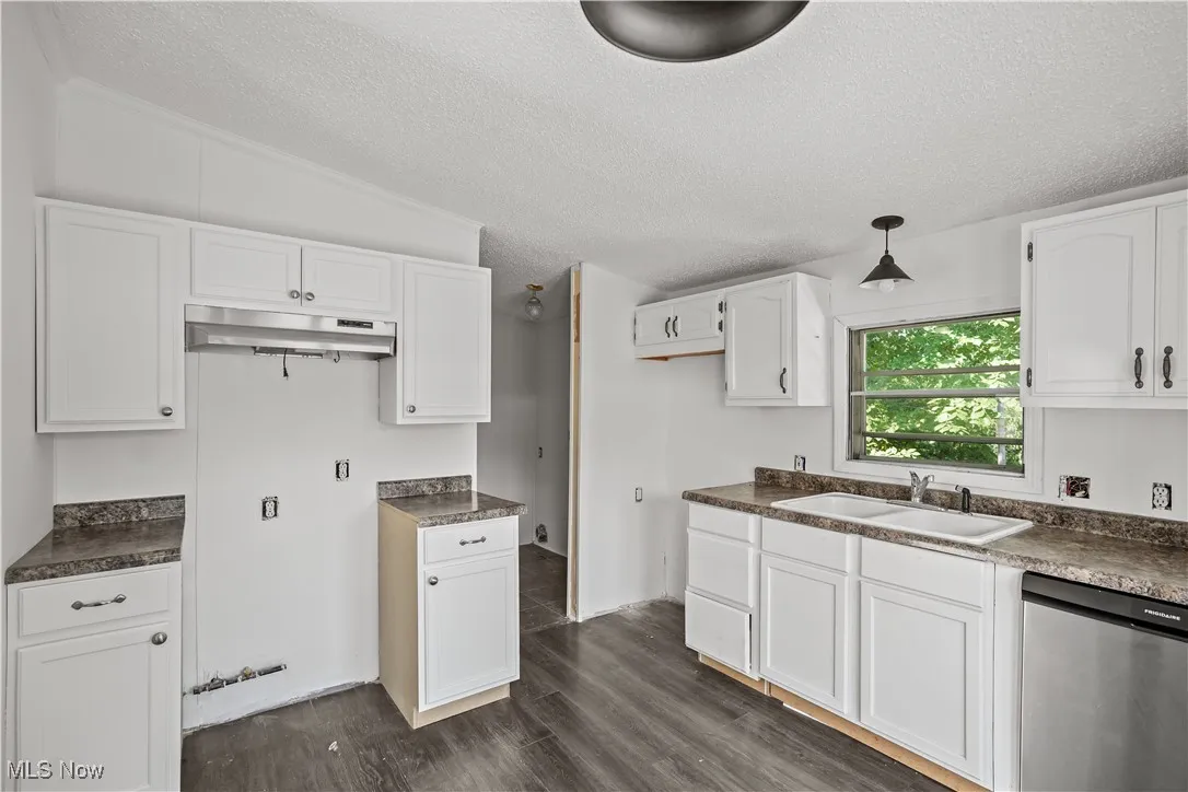 Kitchen with dishwasher, dark countertops, a textured ceiling, dark wood-style flooring, and white cabinetry