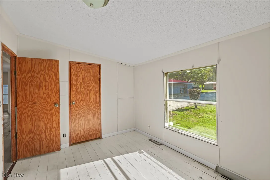 Unfurnished bedroom featuring a closet, lofted ceiling, a textured ceiling, light wood-style flooring, and ornamental molding