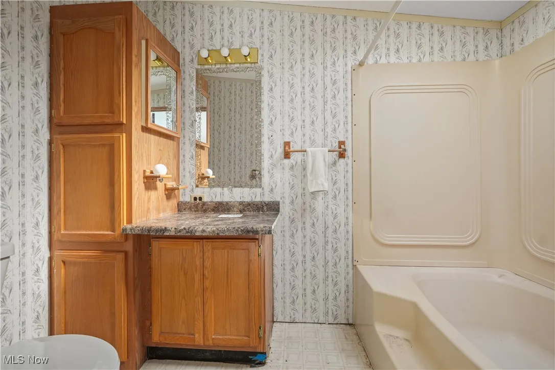 Full bath featuring vanity, wallpapered walls, light flooring, and tub / shower combination