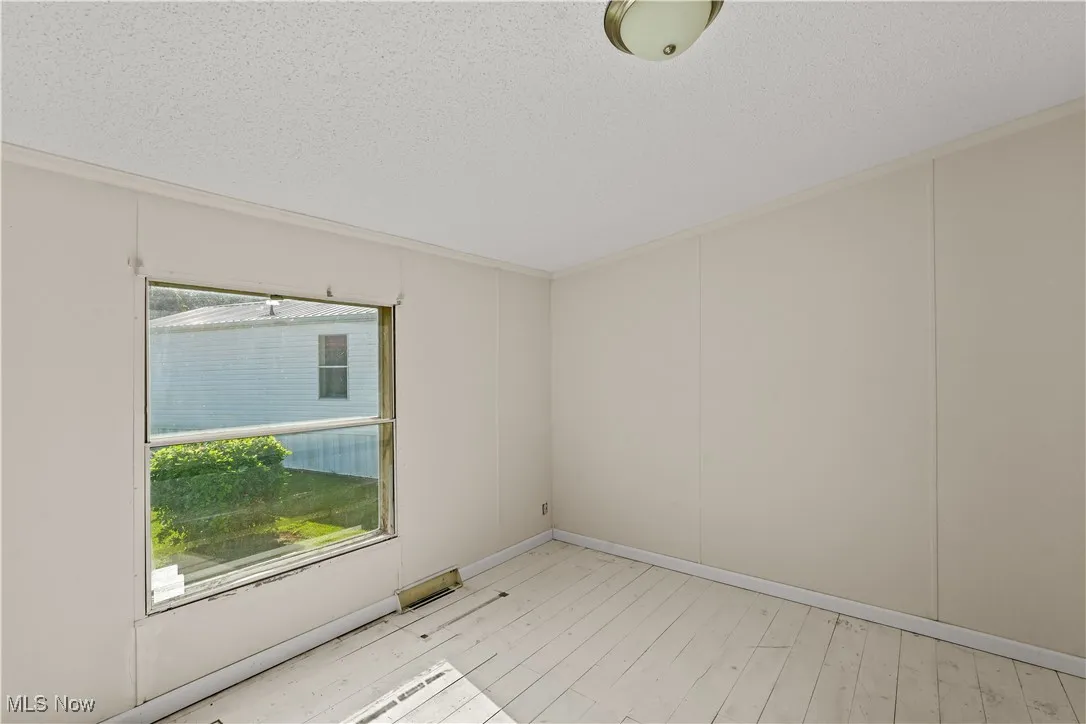 Unfurnished room featuring light wood-style floors, a textured ceiling, and ornamental molding