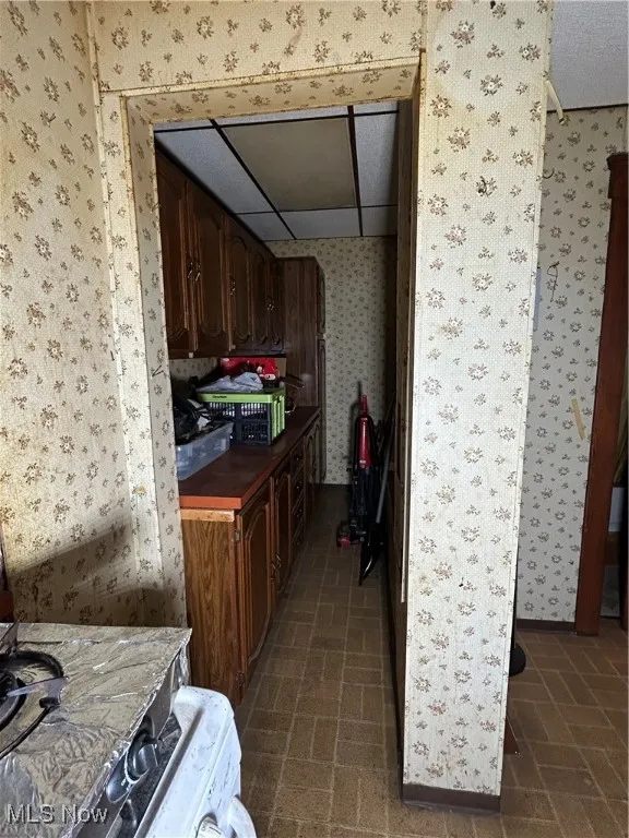 Kitchen featuring wallpapered walls, brick patterned floors, dark brown cabinets, and washer / clothes dryer