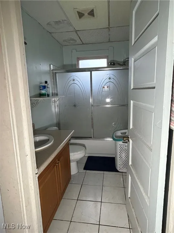 Full bathroom with bath / shower combo with glass door, vanity, a paneled ceiling, and light tile patterned flooring