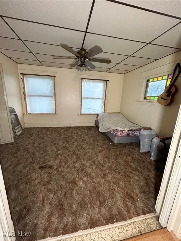 Unfurnished bedroom featuring a paneled ceiling, ceiling fan, and dark colored carpet