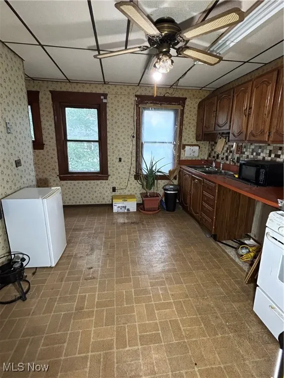 Kitchen with brick patterned flooring, dark countertops, a paneled ceiling, a ceiling fan, and stove