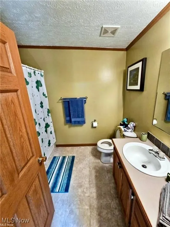 Bathroom featuring a textured ceiling, vanity, crown molding, and tile patterned floors