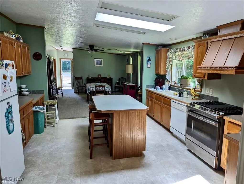 Kitchen with appliances, ceiling fan, a center island, brown cabinetry, and a textured ceiling