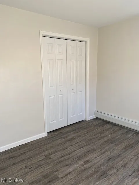 Unfurnished bedroom featuring dark wood-style floors, a baseboard heating unit, and a closet