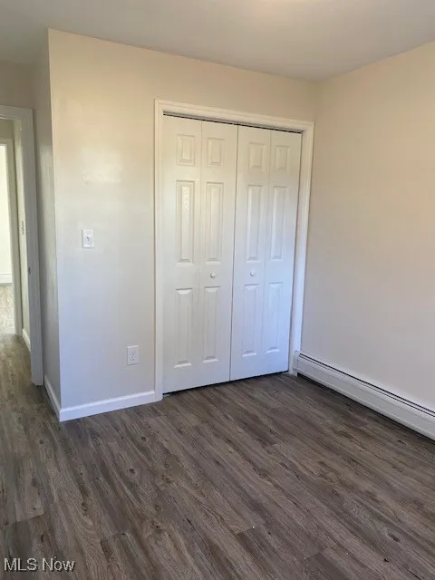 Unfurnished bedroom with a baseboard radiator, dark wood-style floors, and a closet