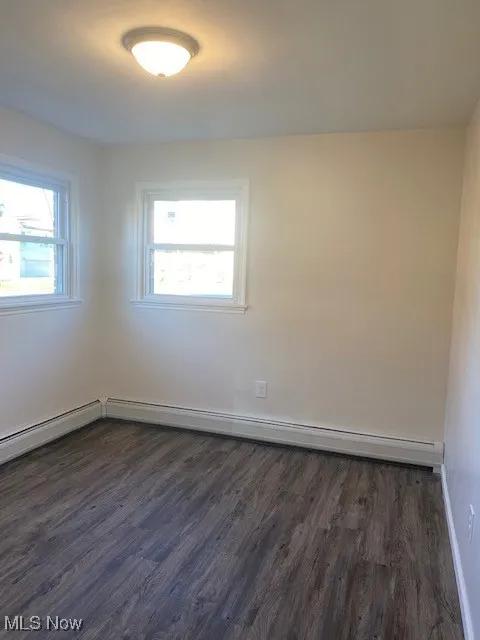 Unfurnished room featuring dark wood finished floors and a baseboard radiator