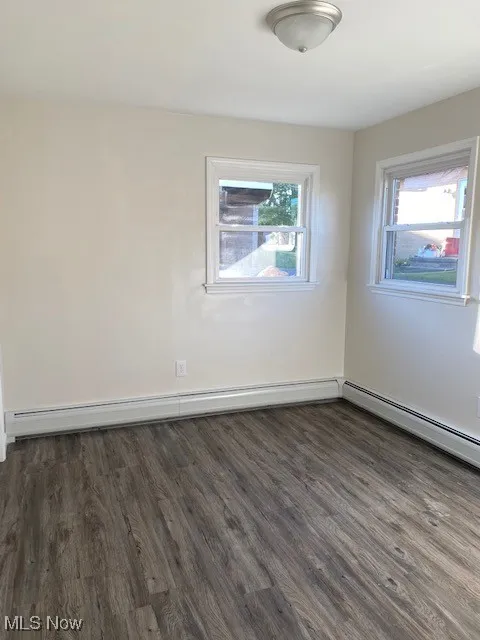 Empty room featuring dark wood-style floors and a baseboard heating unit