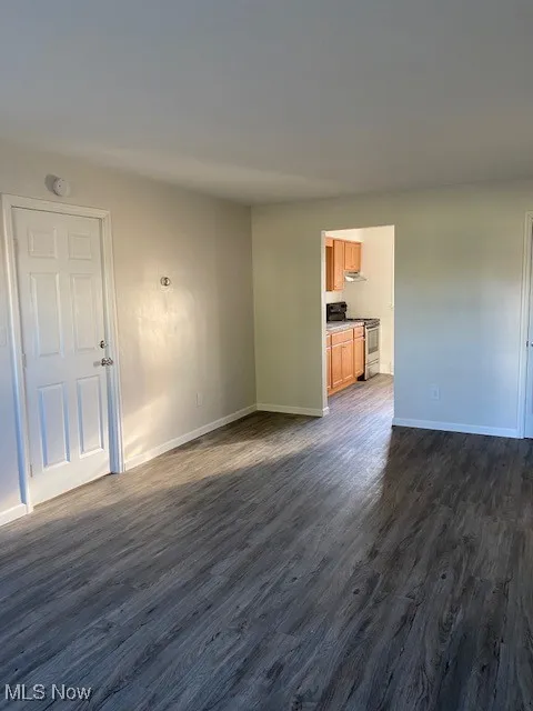 Unfurnished living room with dark wood-type flooring and baseboards
