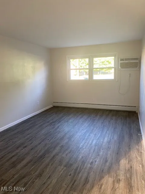 Spare room with dark wood-style floors, a baseboard heating unit, and a wall unit AC