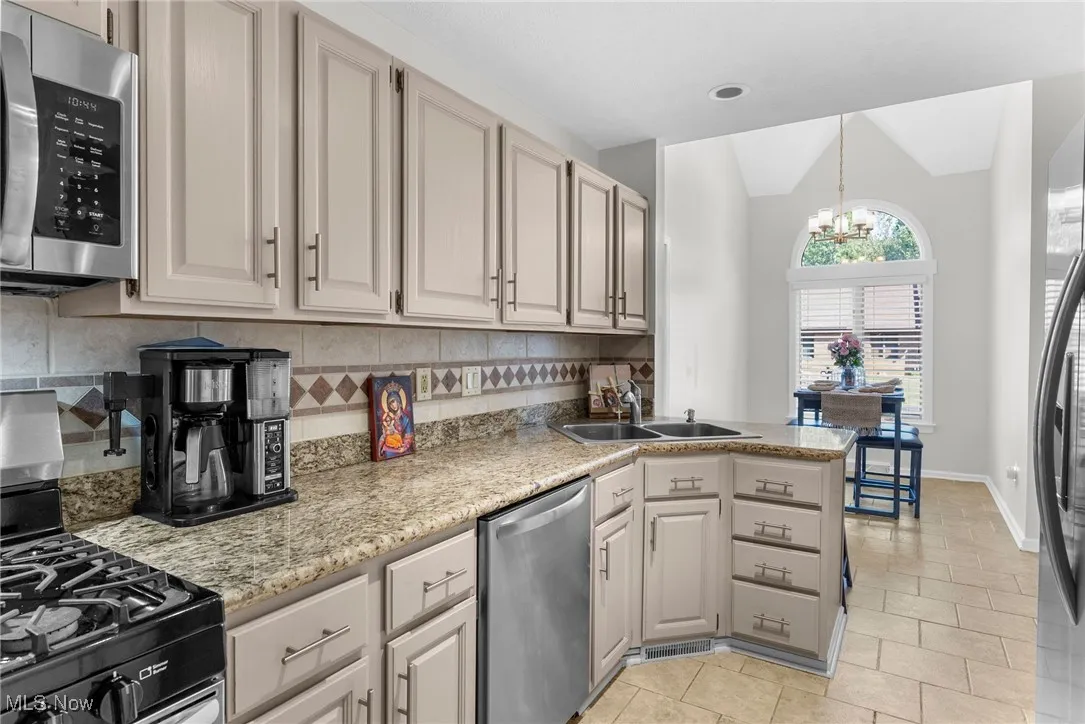 Kitchen featuring appliances with stainless steel finishes, decorative backsplash, a chandelier, decorative light fixtures, and a peninsula